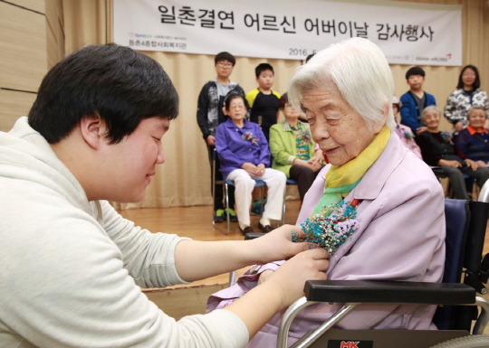 아시아나항공 직원 자녀가 지난 7일 강서구 등촌4종합사회복지관에서 진행된 ‘사랑의 카네이션’ 달아주기 행사 중 결연을 맺은 독거 어르신들의 가슴에 카네이션 꽃을 달아드리고 있다. 아시아나항공은 임직원들이 2012년부터 관내 독거노인 댁을 찾아 산책·안마·목욕·식사 등의 봉사활동을 해오고 있다. /사진제공=아시아나항공