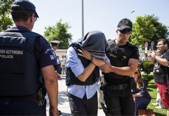 21일(현지시간) 그리스 알렉산드로폴리스 법원에서 불법입국 혐의로 기소된 터키 군인(가운데)이 얼굴을 가린채 경찰의 안내를 받으며 걸어가고 있다. /알렉산드로폴리스=AFP연합뉴스