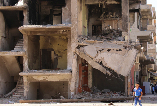 지난 13일(현지시간)시리아 북동부 카미실리에서 한 어린이가 장난감 총을 들고 무너진 건물 옆을 지나가고 있다. 러시아와 미국은 12일 자정을 기해 휴전에 합의했다. /카미실리=AFP연합뉴스