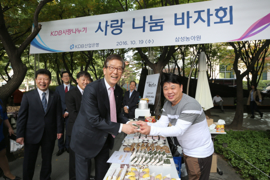 이동걸(왼쪽) 산업은행 회장이 19일 서울 여의도 산은 본점 앞에서 열린 사랑나눔바자회에서 사회적기업인 ‘떡 프린스’ 판매직원과 악수를 하고 있다./사진제공=산업은행