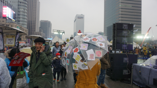 19일 4차 범국민행동에 경찰 차벽을 가득 메웠던 ‘꽃 스티커’를 우산에 붙이고 한 시민이 행진에 동참하고 있다.