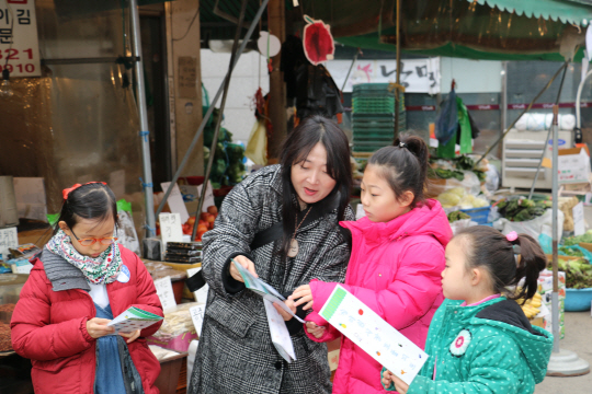 26일 ‘문화예술 명예교사 사업-특별한 하루’ 프로그램에 참가한 서울 수유동 아이들이 명예교사 나난(왼쪽 두번째)과 함께 인근 장미원시장에서 자신들이 그린 ‘보물’들을 찾고 있다. 과일·채소가게에 걸려있는 ‘사과’ 그림이 뒤쪽에 보인다.