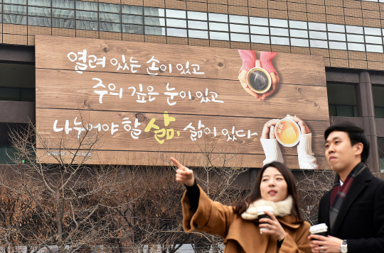 시민들이 5일 광화문글판 겨울편이 걸린 서울 종로구 교보생명 본사 사옥 앞을 지나가고 있다. 광화문글판 겨울편은 프랑스 시인 폴 엘뤼아르의 ‘그리고 미소를(Et un sourire)’에서 가져왔다. 바쁜 일상 속에 미처 돌아보지 못한 주변을 살피고 먼저 손 내밀어 희망을 나누며 살아가자는 메시지를 담았다는 게 교보생명 측 설명이다./사진제공=교보생명