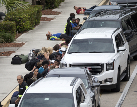 지난 6일(현지시간) 총기난사 사건이 발생한 미국 플로리다주 포트로더데일 국제공항에서 사람들이 총격을 피해 주차된 차량 뒤로 몸을 숨긴 채 대기하고 있다. 이날 총격으로  최소 5명이 목숨을 잃었으며 퇴역군인 출신 용의자는 현장에서 체포됐다.  /포트로더데일=AP연합뉴스