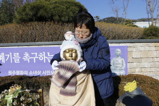 지난 11일 원주시청공원 내 ‘원주 평화의 소녀상’ 앞에서 열린 월례 수요집회에 앞서 원주시민연대 이선경 대표가 소녀상 목에 털목도리를 둘러주고 있다. 소녀상의 손에는 이름 모를 시민들이 쥐어준 핫팩들도 놓여 있다. 2015년 8월 건립된 원주 소녀상은 전국 최초로 원주시 공공조형물로 등록돼 모범적으로 관리되고 있다. /연합뉴스