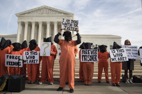 관타나모 수용소 폐쇄를 요구하는 시위대가 지난 11일(현지시간) 미국 워싱턴DC의 미국 연방대법원 앞에서 수감자 복장을 입고 피켓을 들고 있다.  /워싱턴DC=EPA연합뉴스