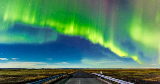 남 아이슬란드 비크 근처의 도로 위에 펼쳐진 북극 오로라. 아이슬란드의 긴 겨울 밤에 흔히 볼 수 있는 풍경이다.
