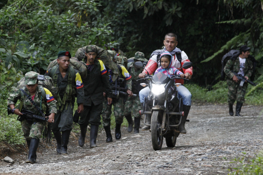 1월31일(현지시간) 콜롬비아 남서부 카우카주 로블의 비무장지대로 향하는 최대 반군 콜롬비아무장혁명군(FARC) 병사들 옆으로 오토바이에 아이를 태운 한 시민이 지나가고 있다. 정부와 평화협정을 체결한 FARC가 이날부터 무장해제에 돌입함에 따라 6,300명에 달하는 대원들은 전국 26곳의 비무장지대로 집결한 후 무기를 반납하고 사회에 복귀한다. 콜롬비아 정부는 제2반군인 민족해방군(ELN)과의 공식 평화협상도 다음달 7일부터 진행할 계획이다./로블=EPA연합뉴스