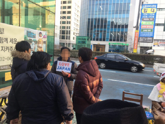 부산 일본영사관 앞에 설치된 소녀상 주변에 한 남성이 소녀상 철거를 요구하는 불법 부착물을 붙여 소녀상 지킴이 단체와 갈등을 빚고 있다. 한 남성이 ‘LOVE JAPAN’이라고 쓴 종이를 들고 소녀상 철거 1인 시위를 벌이고 있다. /연합뉴스