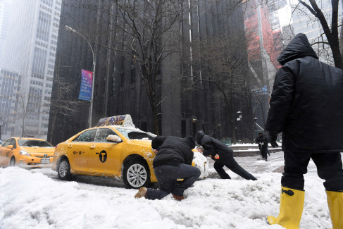14일(현지시간) 미국 뉴욕시 맨해튼에서 사람들이 눈 속에 갇힌 택시를 빼내기 위해 힘을 쓰고 있다. /뉴욕=AFP연합뉴스