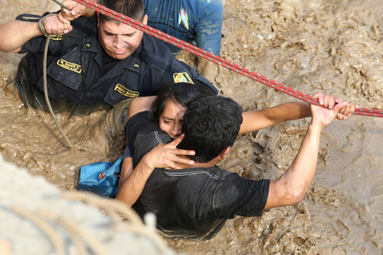 REFILE - CORRECTING NAME OF THE RIVER A woman is assisted while crossing a flooded street after the Huaycoloro river overflooded its banks sending torrents of mud and water rushing through the streets in Huachipa, Peru, March 17, 2017. REUTERS/Guadalupe Pardo      <저작권자(c) 연합뉴스, 무단 전재-재배포 금지>