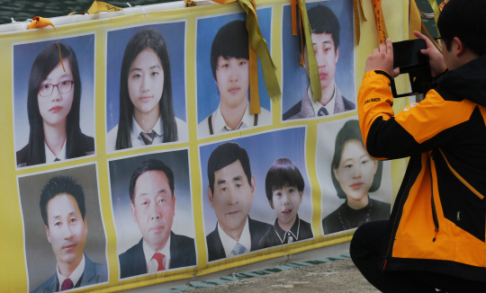 지난 24일 한 추모객이 전남 진도군 팽목항 걸림막에 있는 미수습자 9명의 사진을 휴대폰에 담고 있다. /진도연합뉴스