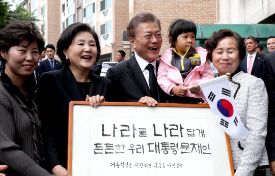 문재인 대통령과 부인 김정숙 여사가 10일 오전 서울시 서대문구 홍은동 자택을 나서며 ‘나라를 나라답게 든든한 우리 대통령 문재인’ 글자가 쓰인 액자를 받고 밝게 웃고 있다./연합뉴스