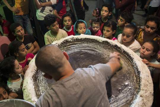 이슬람교의 금식 성월인 라마단에 주로 먹는 전통과자인 ‘쿠나파’를 만드는 모습을 이집트 카이로에서 25일(현지시간) 아이들이 지켜보고 있다. 라마단은 오는 27일부터 시작된다.   /카이로=EPA연합뉴스
