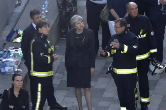 테레사 메이 영국 총리(가운데)가 화재가 발생한 런던 시내 고층아파트 ‘그렌펠 타워’를 방문, 소방당국의 설명을 듣고 있다. 이번 화재가 ‘예고된 인재’라는 여론 속에 메이 총리에 대한 비판이 커지고 있다. /연합뉴스