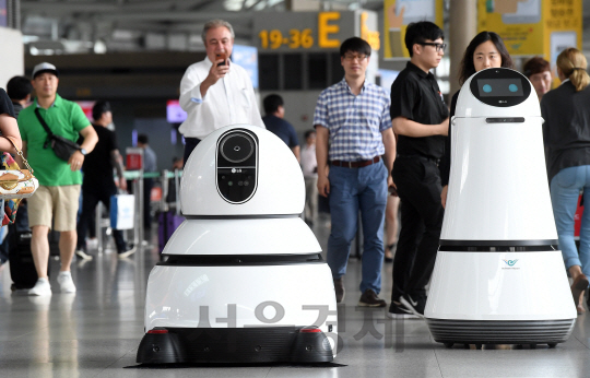 인천국제공항에서  LG전자의 상업용 로봇 시범서비스 시작 첫날인 21일 여행객들이 신기한 표정으로 안내로봇(오른쪽) 과 청소로봇을 구경하고 있다./영종도=이호재기자.