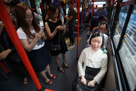 서울 시내버스 151번 버스 승객들이 14일 ‘세계 위안부 기림일’을 맞아 버스 좌석에 설치된 ‘평화의 소녀상’을 휴대폰에 담고 있다.  /연합뉴스