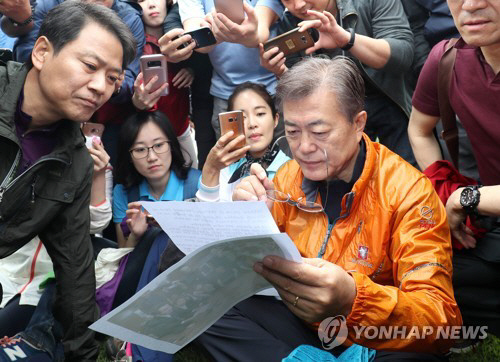 문재인 대통령이 당선 후 첫 주말인 지난 5월 13일 기자들과 산행 전 청와대 경내에서 임종석 대통령 비서실장이 전한 세월호 미수습자 가족들이 보낸 편지를 읽고 있다. /연합뉴스