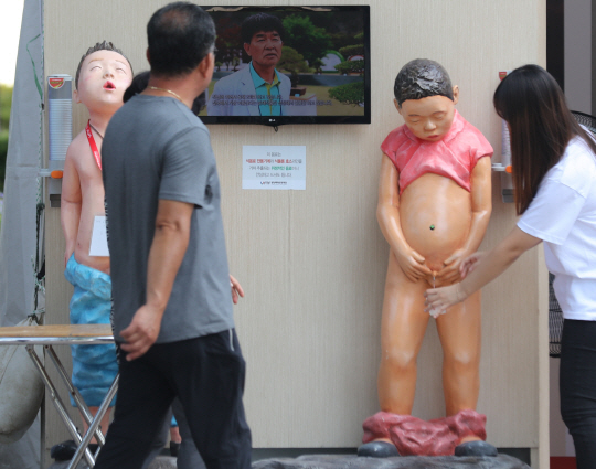 한 시민이 ‘벗은 아동’ 모습의 아동의 ‘고추’에서 흘러나오는 물을 받고 있다. /연합뉴스