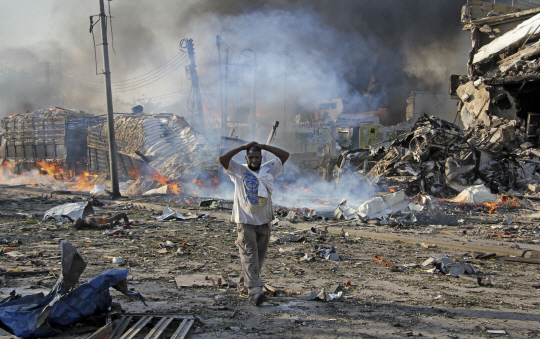 A Somali gestures as he walks past a dead body, left, and destroyed buildings at the scene of a blast in the capital Mogadishu, Somalia Saturday, Oct. 14, 2017. A huge explosion from a truck bomb has killed at least 20 people in Somalia‘s capital, police said Saturday, as shaken residents called it the most powerful blast they’d heard in years. (AP Photo/Farah Abdi Warsameh)      <저작권자(c) 연합뉴스, 무단 전재-재배포 금지>