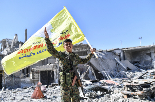 쿠르드·아랍연합 ‘시리아민주군’(SDF) 소속 군인이 17일(현지시간) 이슬람국가(IS)의 상징적 수도 시리아 락까를 장악한 뒤 승리를 의미하는 깃발을 흔들고 있다. /락까=AFP연합뉴스