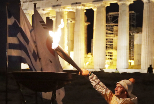 그리스의 올림픽 체조 금메달리스트인 디모스테니스 탐파코스가 지난 10월30일 그리스 아테네의 파르테논 신전 앞에 설치된 성화대에 불꽃을 옮기고 있다. 이 불꽃은 평창올림픽 조직위원회에 인수돼 11월1일 국내에 입성한다. /아테네=AP연합뉴스