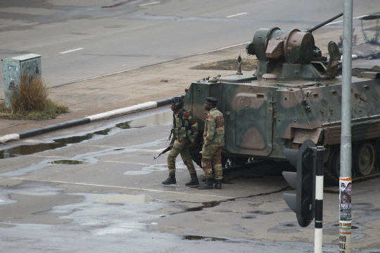 짐바브웨 군부가 국영방송사를 장악한 이튿날인 15일(현지시간) 수도인 하라레에서 정차된 탱크 앞으로 무장 군인들이 지나가고 있다. /하라레=AP연합뉴스