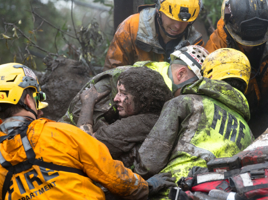 미국 로스앤젤레스(LA) 북서쪽 몬테시토에서 9일(현지시간)구조대원들이 무너진 가옥 잔해와 진흙더미에 파묻혔던 여성을 구출하고 있다./몬테시토=AP연합뉴스