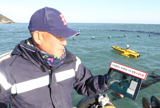 한 어민이 부산 해운대 송정리 포구에서 바다에 떠 있는 수상드론이 수집한 양식장 환경 정보를 태블릿를 통해 확인하고 있다. /사진제공=LG유플러스