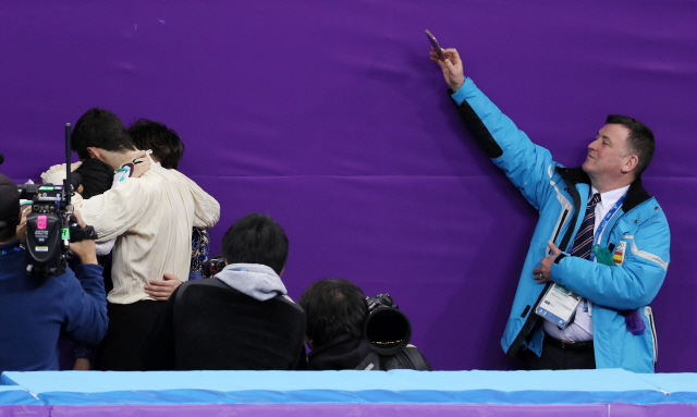 17일 강릉아이스아레나에서 열린 2018 평창동계올림픽 피겨 남자 싱글 프리스케이팅 경기 직후 브라이언 오서 코치(오른쪽)가 자신의 제자인 하뉴 유즈루와 하비에르 페르난데스가 포옹하는 모습을 멀리서 지켜보며 촬영하고 있다. /연합뉴스