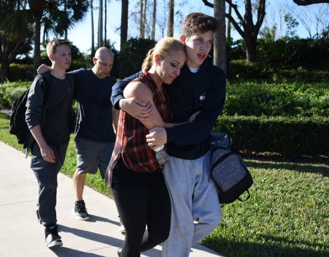 플로리다 파크랜드 마조리 스톤맨 더글러스 고교에서 지난 14일 총격 사건 이후 학생들이 서로를 위로하며 걸어나오고 있다./AFP연합뉴스