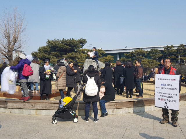 20일 오전 동국대학교 2018년 봄 학위수여식이 열린 가운데 기념사진을 찍는 졸업생들 옆에서 한 동국대 청소노동자가 침묵시위를 벌이고 있다./허세민기자