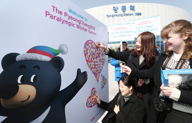 지난 10일 한국방문위원회 대학생 미소국가대표가 평창동계패럴림픽 맞이 환대캠페인의 일환으로 강원도 강릉역 광장에 설치한 ‘반다비’ 포토월 앞에서 내외국인 관광객들이 패럴림픽을 응원하는 스티커를 붙이고 있다. /사진제공=한국방문위원회