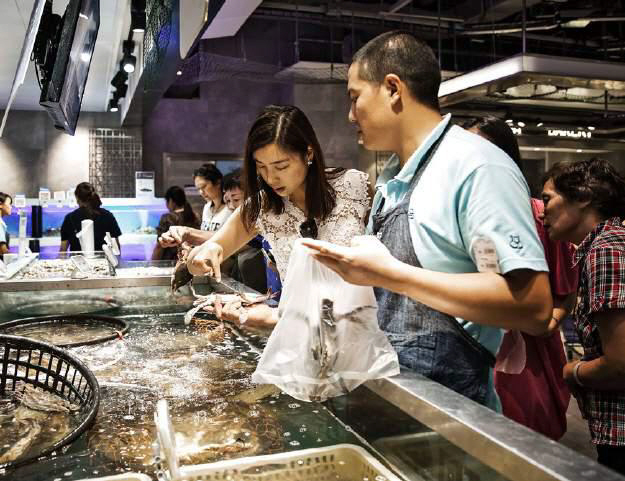 상하이에 위치한 알리바바의 헤마 상점에서 한 직원이 살아있는 해산물을 고르고 있는 고객을 돕고 있다.