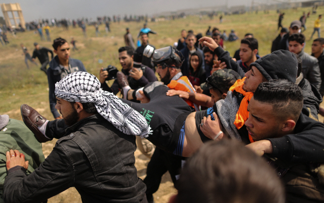 30일(현지시간) 팔레스타인 가자지구 경계선에서 팔레스타인인 시위대들이 이스라엘군의 탱크 발포로 부상 당한 참가자를 옮기고 있다. /가자지구=AFP연합뉴스