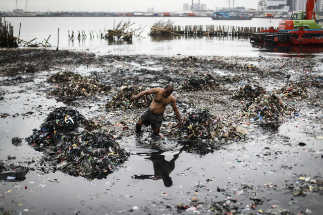 인도네시아 인부가 3월 21일(현지시간) 북자카르타 해안가에 형성된 쓰레기 무덤을 걷고 있다. /자카르타=EPA연합뉴스