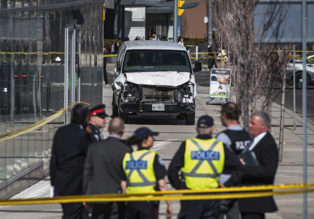 23일(현지시간) 캐나다 토론토 북부 핀치대로에서 인도로 돌진해 사고를 낸 차량 앞에서 경찰들이 수습상황을 논의하고 있다. 이날 사고로 한인 3명을 포함해 10명이 숨지고 15명이 부상했다.   /토론토=AP연합뉴스
