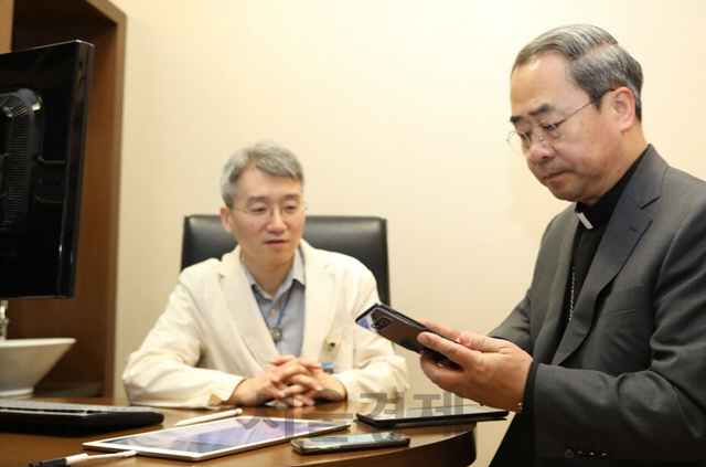 손희송(오른쪽) 가톨릭학원 상임이사(주교)가 11일 서울성모병원 외래진료실에서 스마트폰과 모바일 앱을 이용해 진료 예약~결제 등이 이뤄지는 ‘스마트 병원’을 체험해보고 있다. /사진제공=서울성모병원