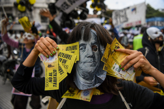 아르헨티나의 수도 부에노스아이레스에서 달러화 가면을 쓴 한 시민이 14일(현지시간) 양손에 페소화 지폐 모양의 종이를 움켜쥐고 아르헨티나 정부와 국제통화기금(IMF)의 구제금융 협상에 반대하는 시위를 벌이고 있다.    /부에노스아이레스=AFP연합뉴스