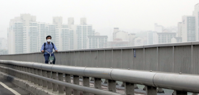 미세먼지와 안개로 흐린 14일 오전 도심에서 한 시민이 마스크를 쓰고 자전거를 타고 있다./연합뉴스