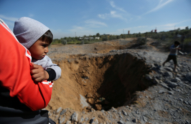 지난 3월 18일(현지시간) 팔레스타인 가자지구에서 한 아이가 부모의 품에 안겨 이스라엘 군의 전투기가 공습한 현장을 쳐다보고 있다. /가자지구=로이터연합뉴스