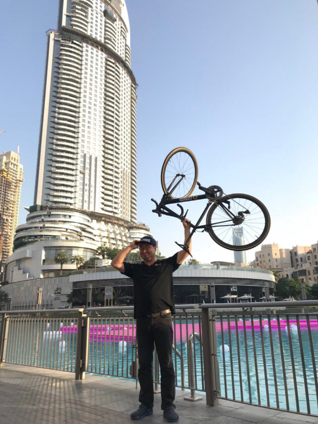 이정훈 스탠다드그래핀 대표가 세계 최고층 빌딩인 두바이 부르즈 칼리파 앞 광장에서 직접 제작한 그래핀 자전거를 한손으로 가볍게 들어 올리고 있다.