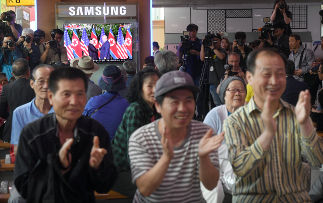 12일 서울 용산구 서울역 대합실에서 TV 앞에 모인 시민들이 북미 정상회담 장면을 지켜보며 박수를 치고 있다.   /이호재기자
