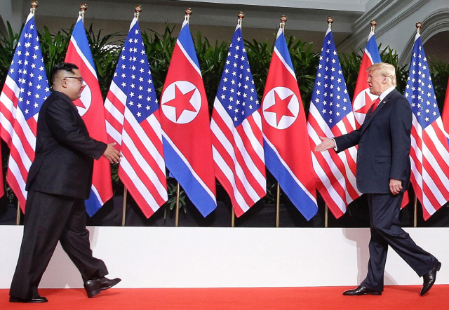 “드디어 만났네요”  김정은(왼쪽) 북한 국무위원장과 도널드 트럼프 미국 대통령이 12일 싱가포르 센토사섬 카펠라호텔에서 열린 북미 정상회담에서 앞서 서로를 향해 손을 내밀며 걸어가고 있다./싱가포르=로이터연합뉴스