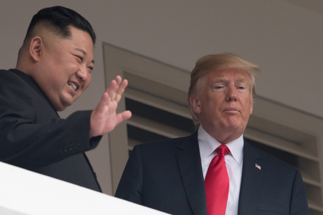 김정은(왼쪽) 북한 국무위원장이 12일(현지시간) 도널드 트럼프 미국 대통령과의 단독 회담을 마치고 확대 회담 참석을 위해 함께 발코니를 걸어가던 도중 취재진을 향해 손을 들어 올리며 웃고 있다.        /싱가포르=AFP연합뉴스