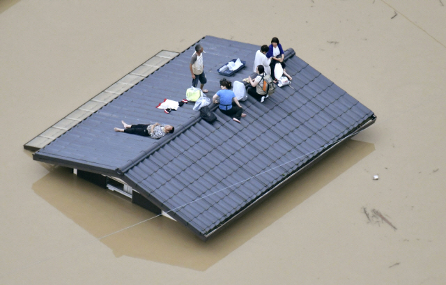 지난 7일 일본 오카야마현 구사시키의 주택가에서 고립된 주민들이 한 가옥의 지붕에 올라가 구조를 기다리는 모습. /연합뉴스