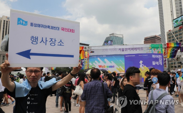 14일 오후 성(性)소수자 축제인 ‘서울퀴어퍼레이드’ 행사가 열린 서울광장 앞에서 한 시민이 대한문 앞에서 열린 퀴어축제 반대집회 안내판을 들고 있다./연합뉴스