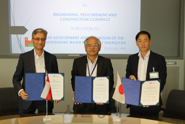 박인원(오른쪽) 두산중공업 Water BG장이 19일 일본 요코하마의 JGC 본사에서 히토시 기타가와(가운데) JGC 인프라 부문장, 자이안타 UIDC 사업개발 부문장과 함께 계약서를 펼쳐보이고 있다./사진제공=두산중공업