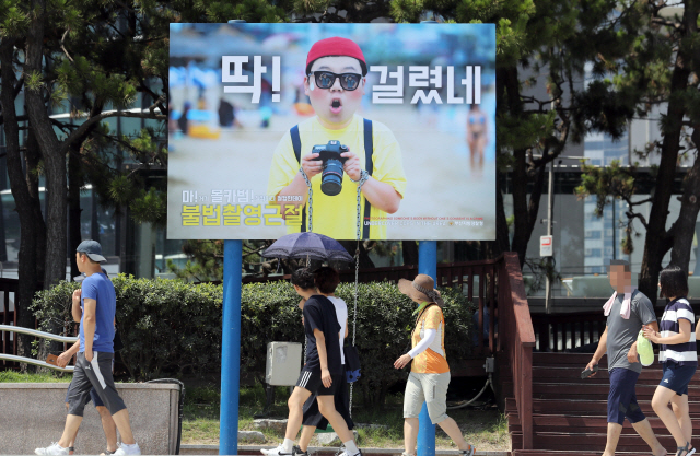 17일 전국 최대 피서 인파가 몰리는 부산 해운대해수욕장에 불법촬영(일명 몰카) 경고 메시지를 담은 ‘불법촬영 근절 이색 그네 광고판’이 설치됐다. 부산경찰청이 설치한 광고판에는 불법촬영 범죄자가 경찰관과 맞닥뜨려 놀라는 모습을 담고 있으며, 경고 문구가 부산 사투리와 영어로 쓰여 있다./연합뉴스