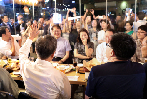 문재인 대통령이 26일 오후 서울 광화문 인근 한 맥줏집에서 퇴근길 시민들과 만나 호프타임을 갖는 동안 시민들이 몰려 지켜보자 손을 들어 인사하고 있다./연합뉴스